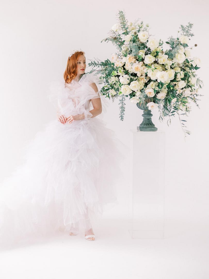 Novia en vestido de novia con volantes junto al arreglo floral